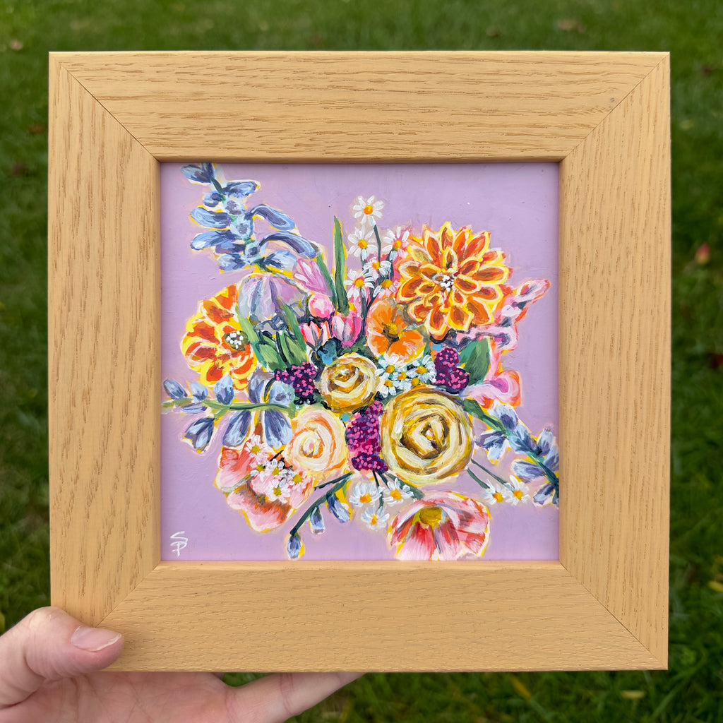 Framed artwork of colorful flowers on a purple background held against a grassy background